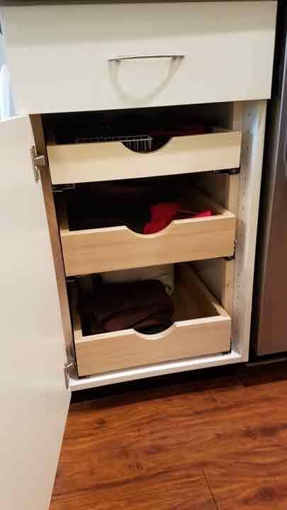Open kitchen cabinet with three pull-out drawers. The drawers are light wood.