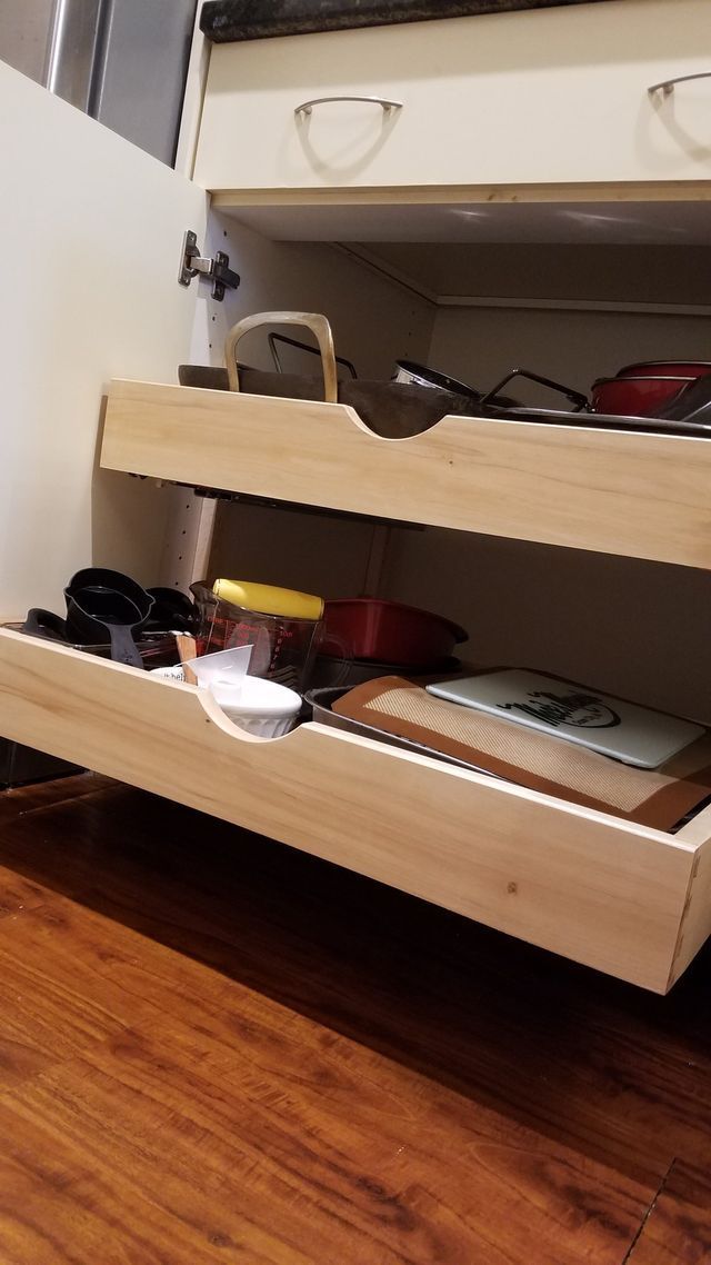 Wooden pull-out shelves in a cabinet, filled with kitchen items. Light wood, partially open.