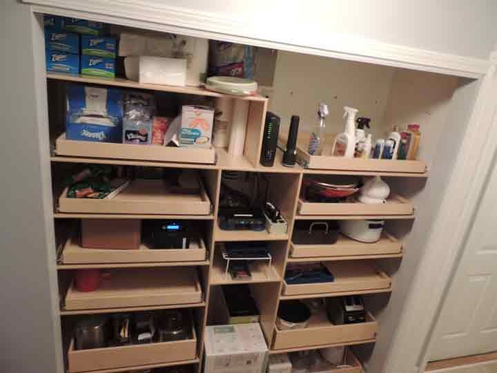 Pantry closet with wood shelves holding various items like food, cleaning supplies, and electronics.