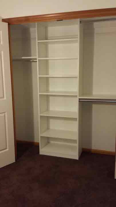 White bookshelf installed inside a closet with a rod on either side; brown carpet and a white door.