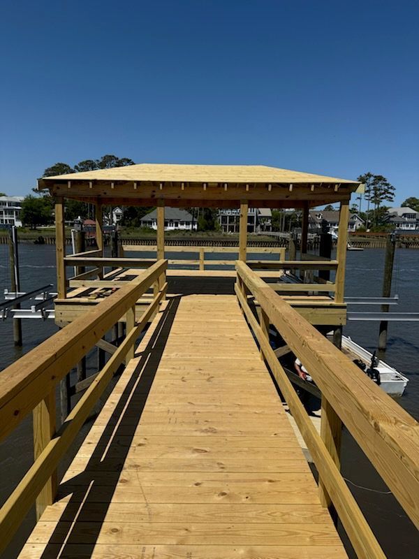 Wooden dock with a covered area over the water, blue sky, and buildings in the distance.