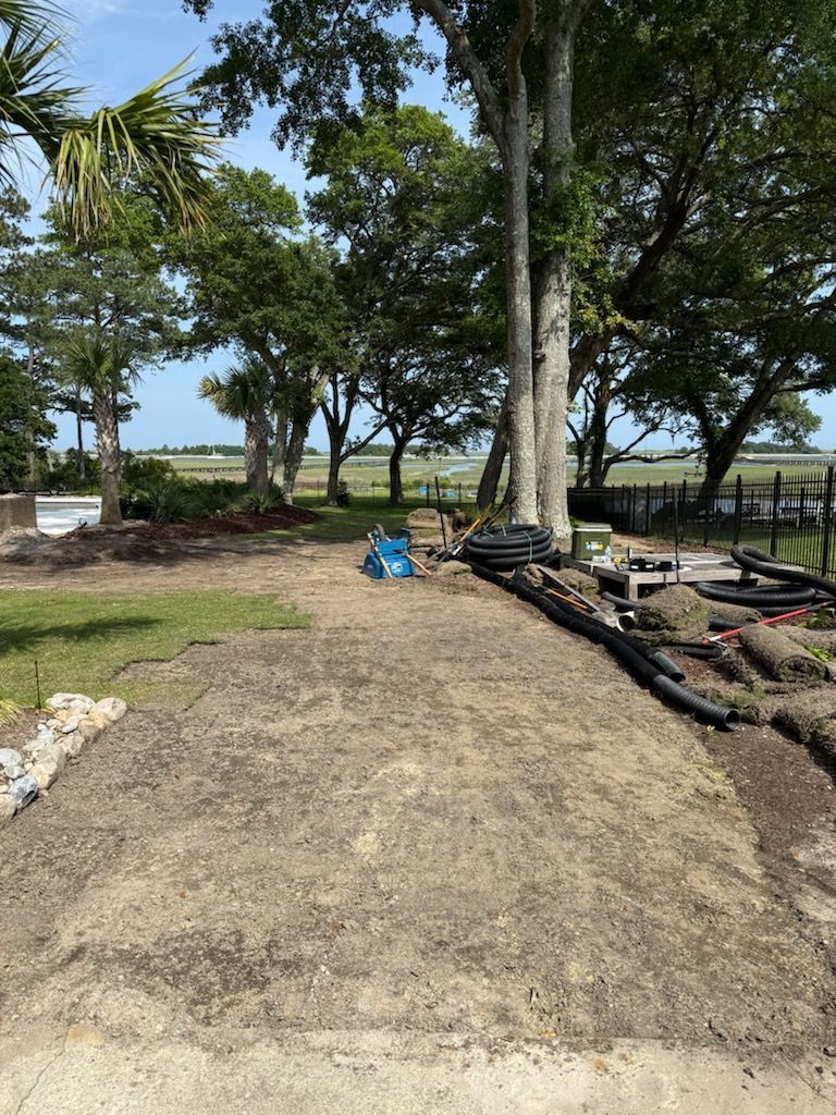 A prepared area with dirt and sod, overlooking a marsh with trees on a sunny day.