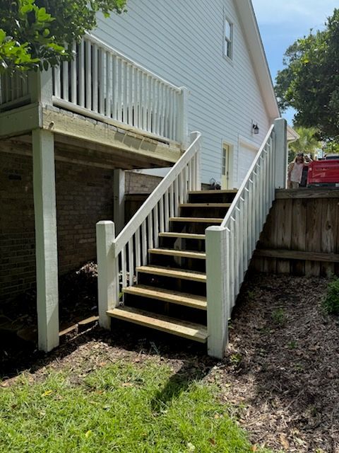 White deck stairs leading up to a house with a white deck and railing, in a yard with grass.