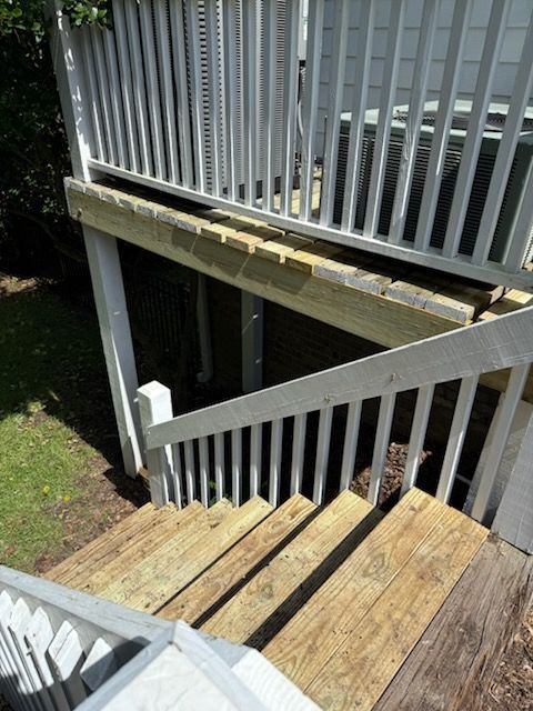 Wooden deck with stairs, white railings, and grey planks, in an outdoor setting.