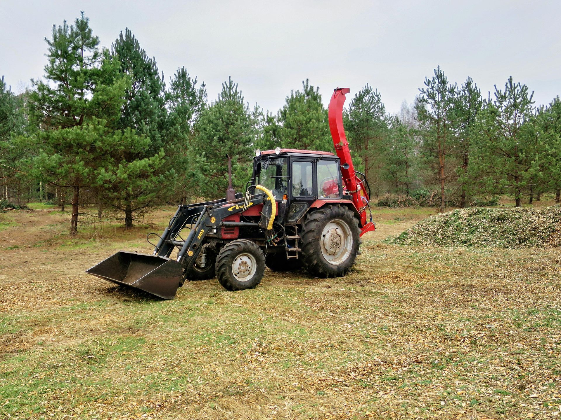 Tractor with front loader and wood chipper in a field with trees.