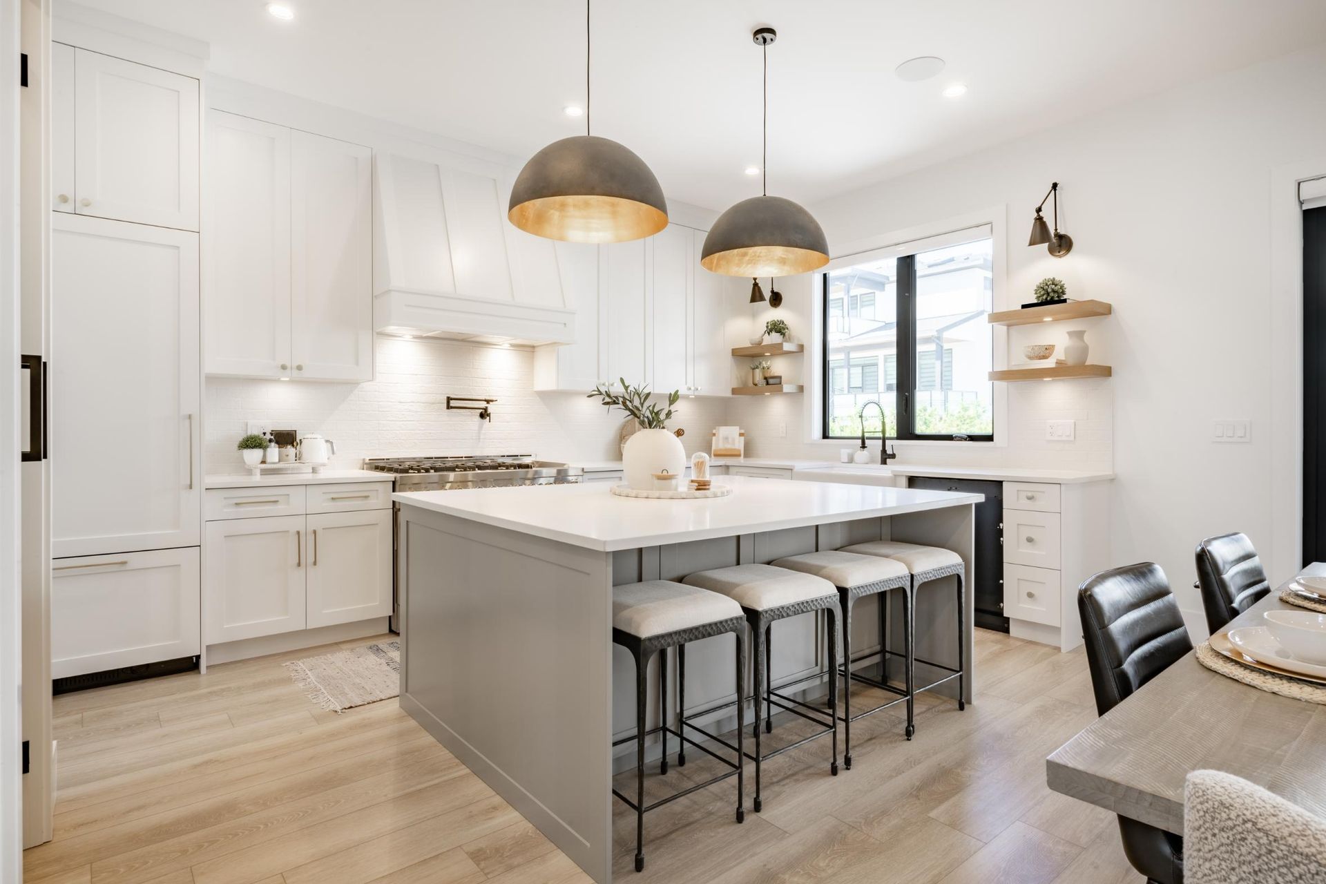 A kitchen with white cabinets, a large island, stools, and a table.