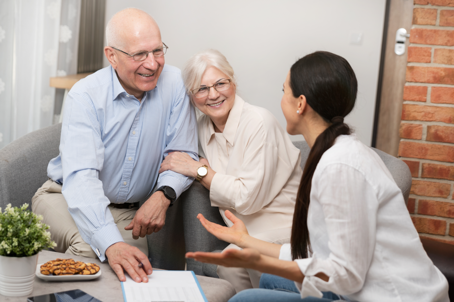 Person in gray blazer holds pen, poised over paperwork at a wooden desk with another person and laptop visible.