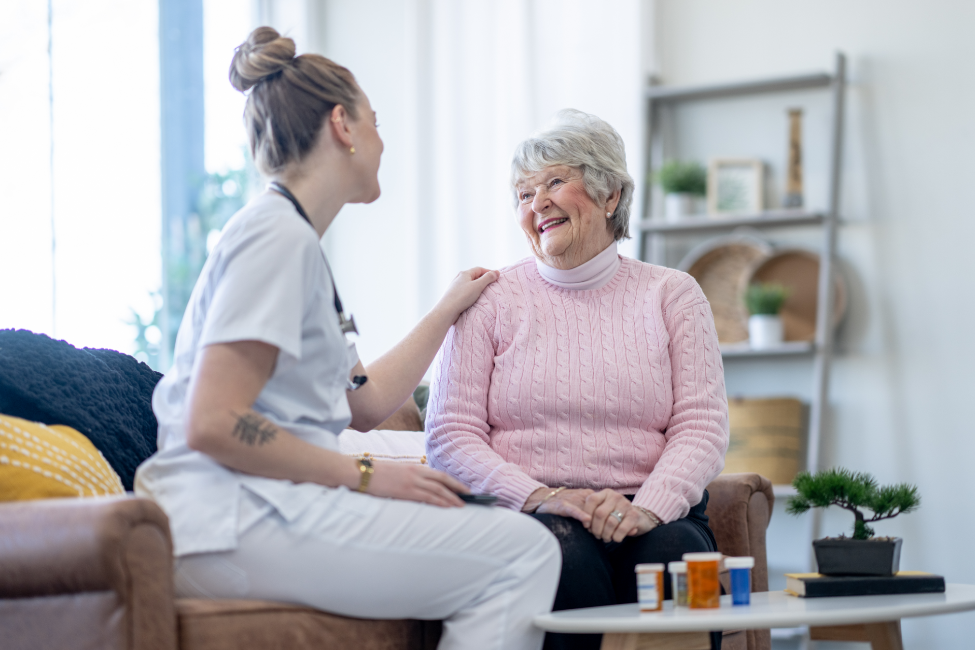 Person in gray blazer holds pen, poised over paperwork at a wooden desk with another person and laptop visible.