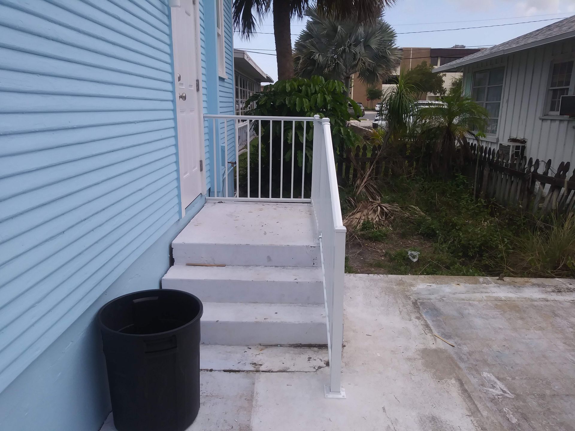 A blue house with white stairs and a black trash can
