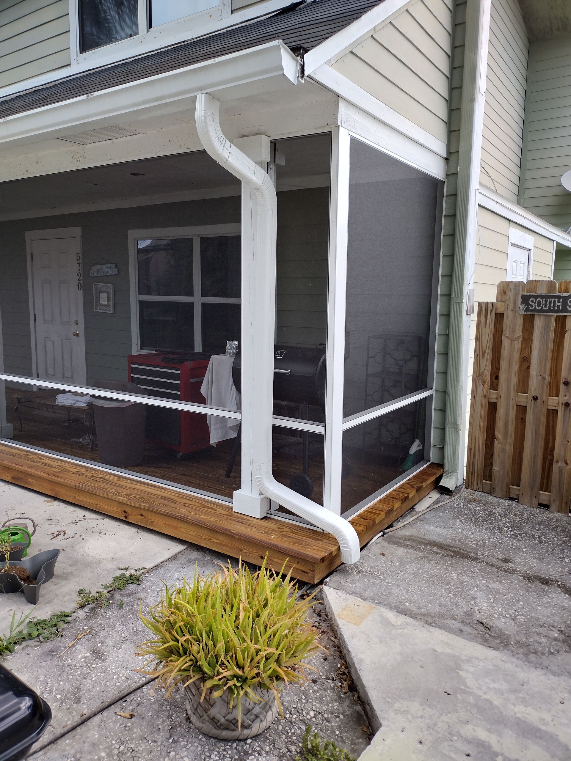 A screened in porch with a white gutter on the side of a house.