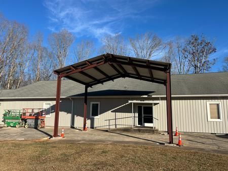 Brown metal carport over a building entrance with a ramp. Orange cones on the ground.
