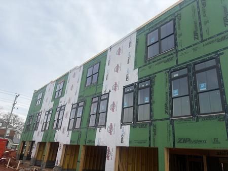 Exterior view of a multi-story building under construction; green sheathing with windows.
