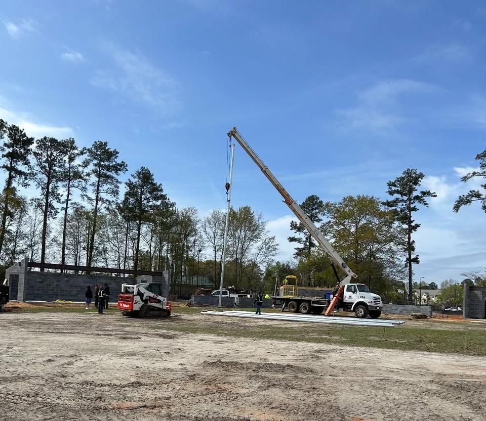 Construction site with a crane lifting a light pole. 