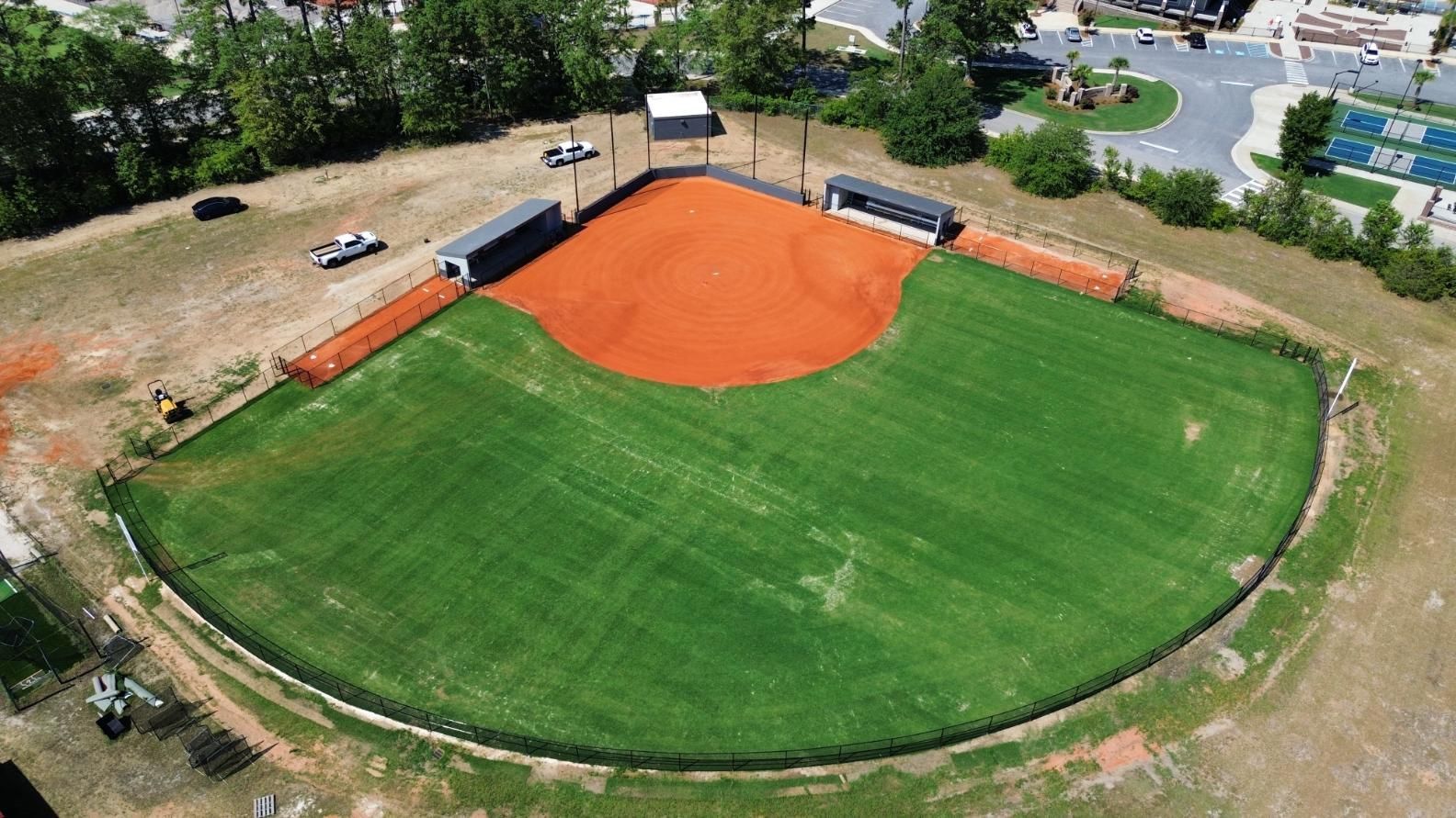 Aerial view of a baseball field with brown infield, green outfield, and small dugouts.