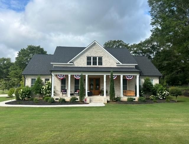 Cream brick house with dark roof, porch swing, and American flag decorations on a green lawn.