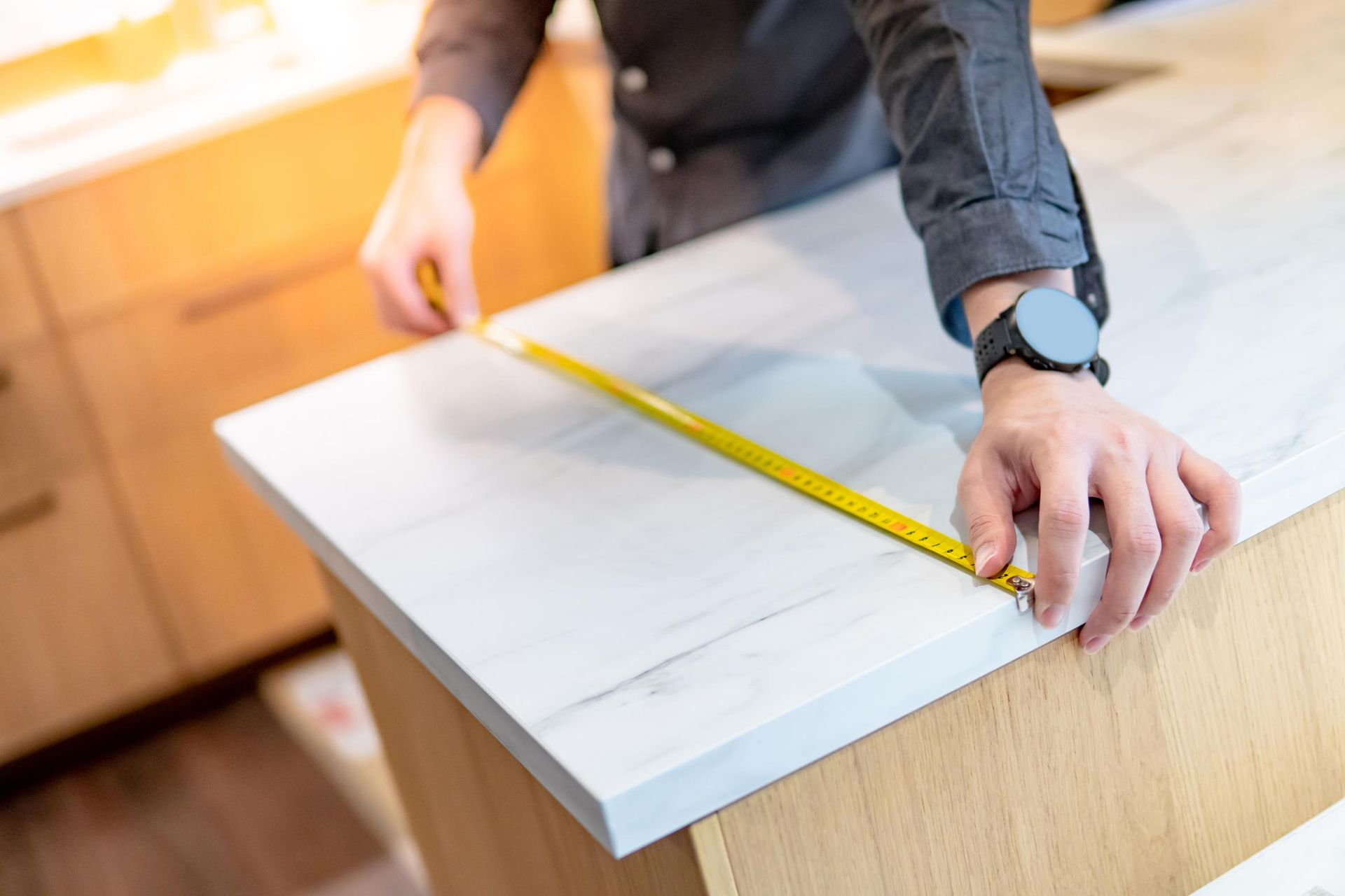 Person measuring a white countertop with a yellow tape measure in a kitchen.