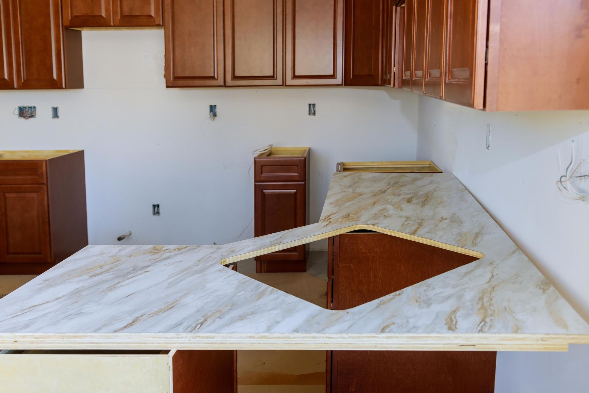 Kitchen with brown cabinets and countertop under construction; light colored countertop with a sink cut out.