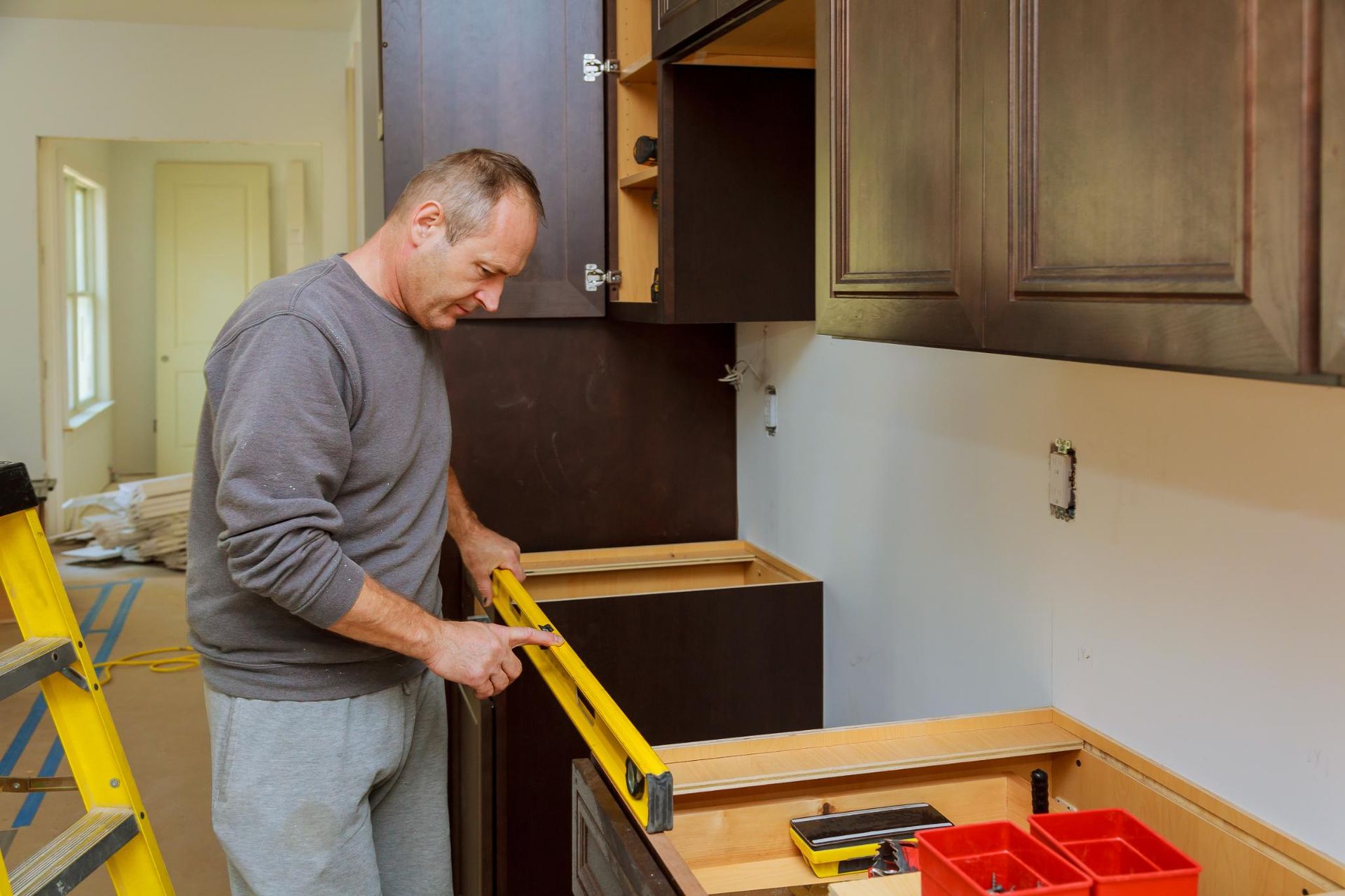 Man using a level to install a kitchen cabinet. Dark brown cabinets, yellow level, neutral interior.