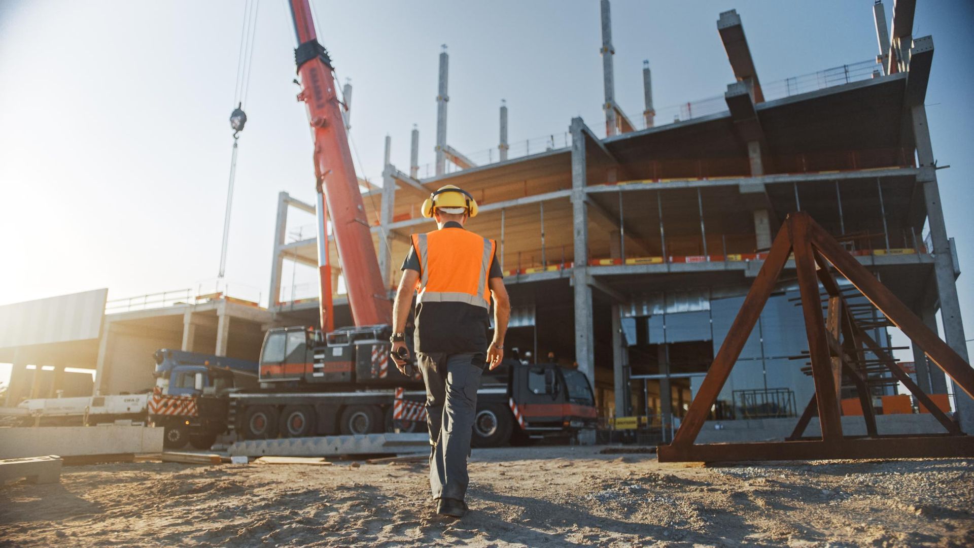 Construction worker walking toward unfinished building, crane operating. 