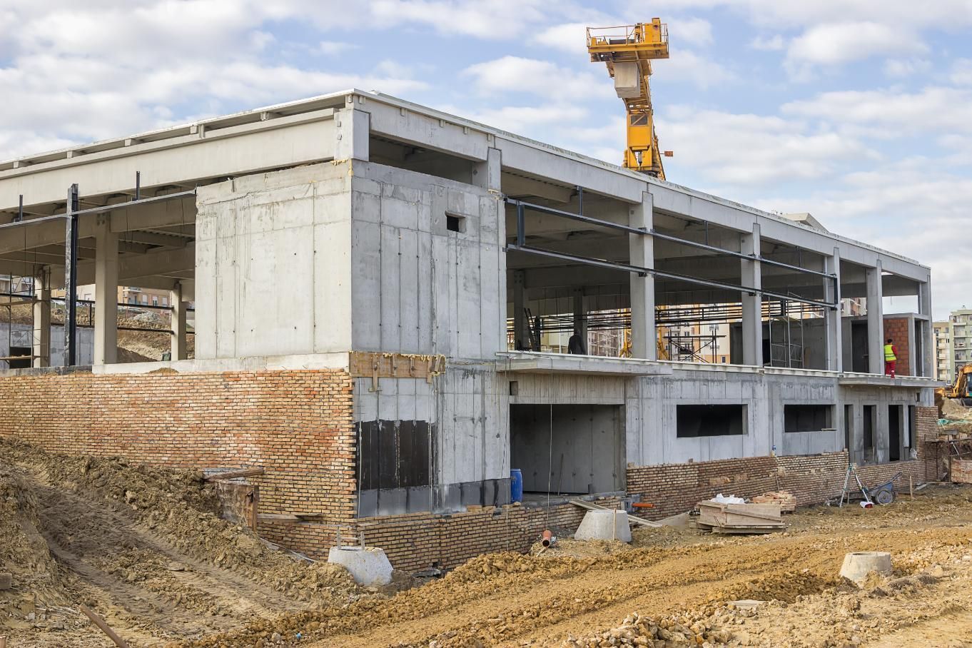 Construction site of a concrete building with a yellow crane and dirt.