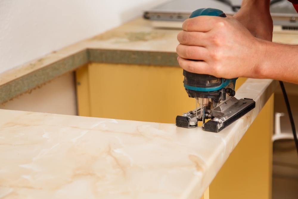 Person using a jigsaw to cut a light-colored countertop in a kitchen.