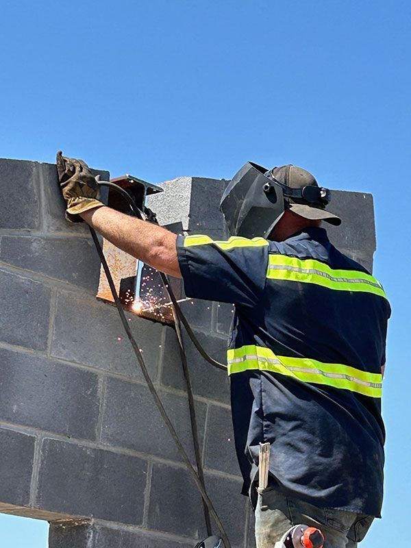 Welder wearing a mask, working on a concrete block wall outdoors.