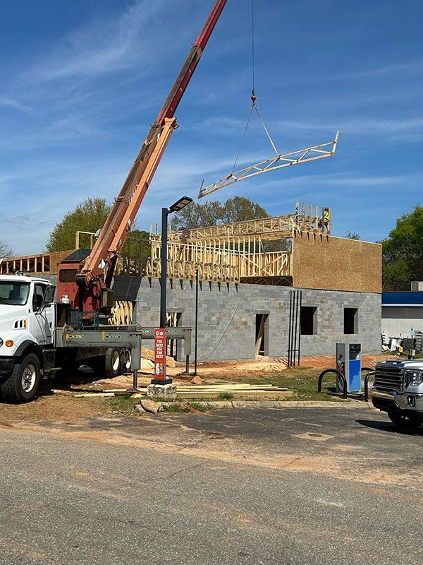 Crane lifting a roof truss onto a building under construction on a sunny day.