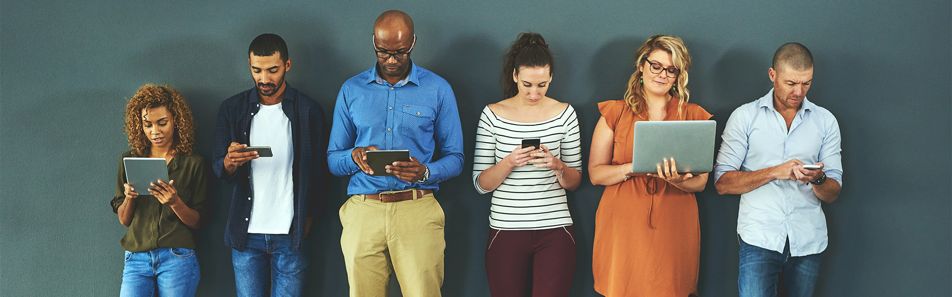 A group of people are standing next to each other looking at their phones.