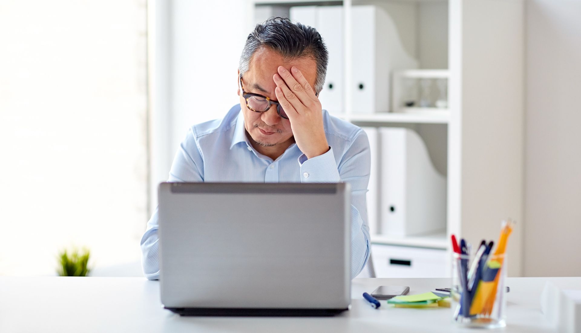 Businessman in eyeglasses with laptop computer suffering from headache at office.