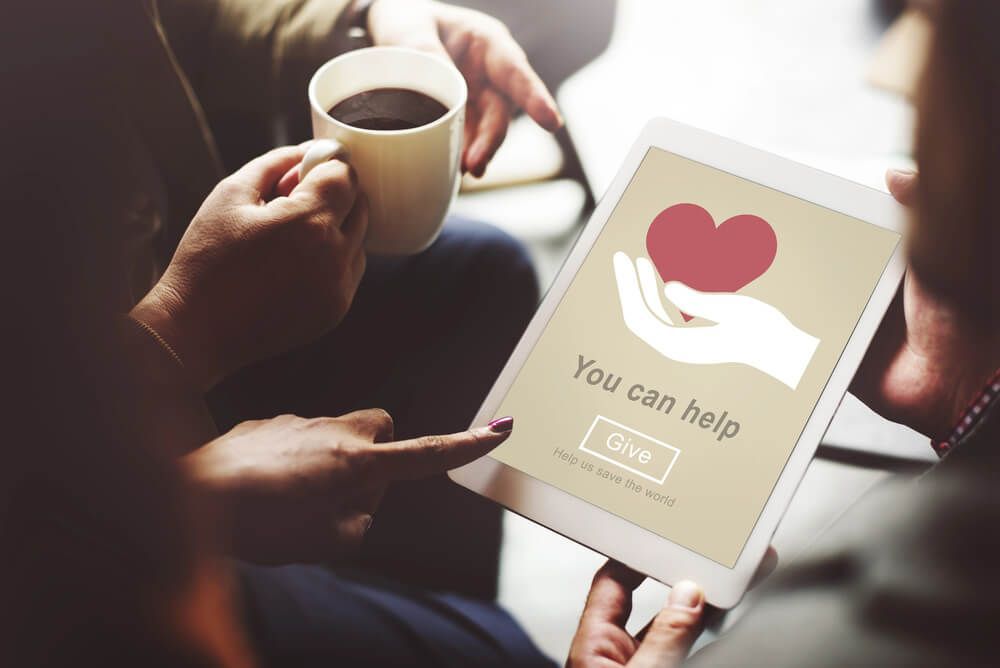 A man is holding a cup of coffee and a tablet with a hand holding a heart on it.