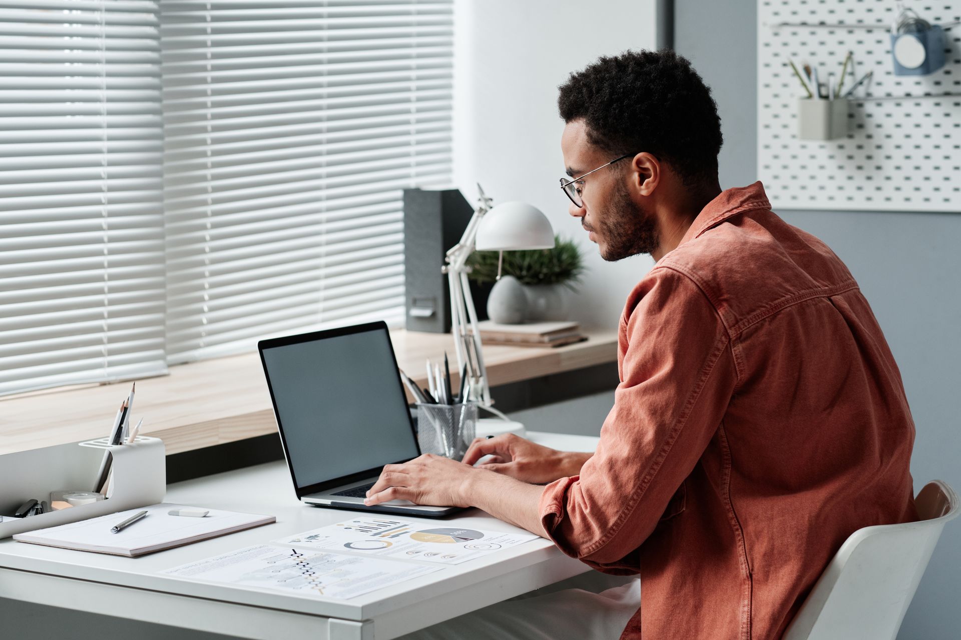 Concentrated young mixed race man sitting at desk and using laptop in office.