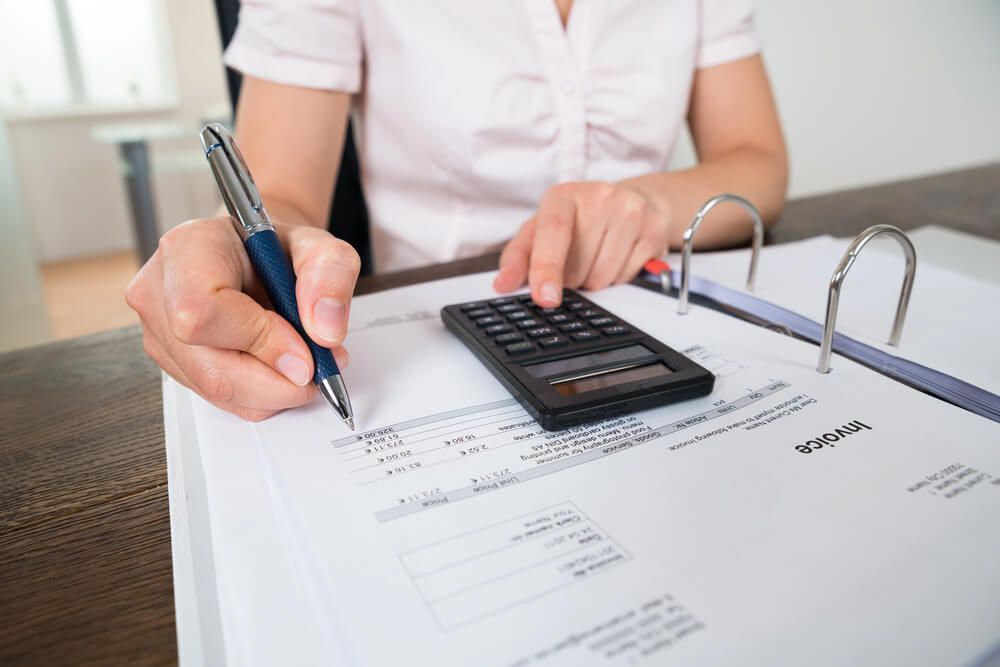 A woman is using a calculator and writing on a piece of paper.