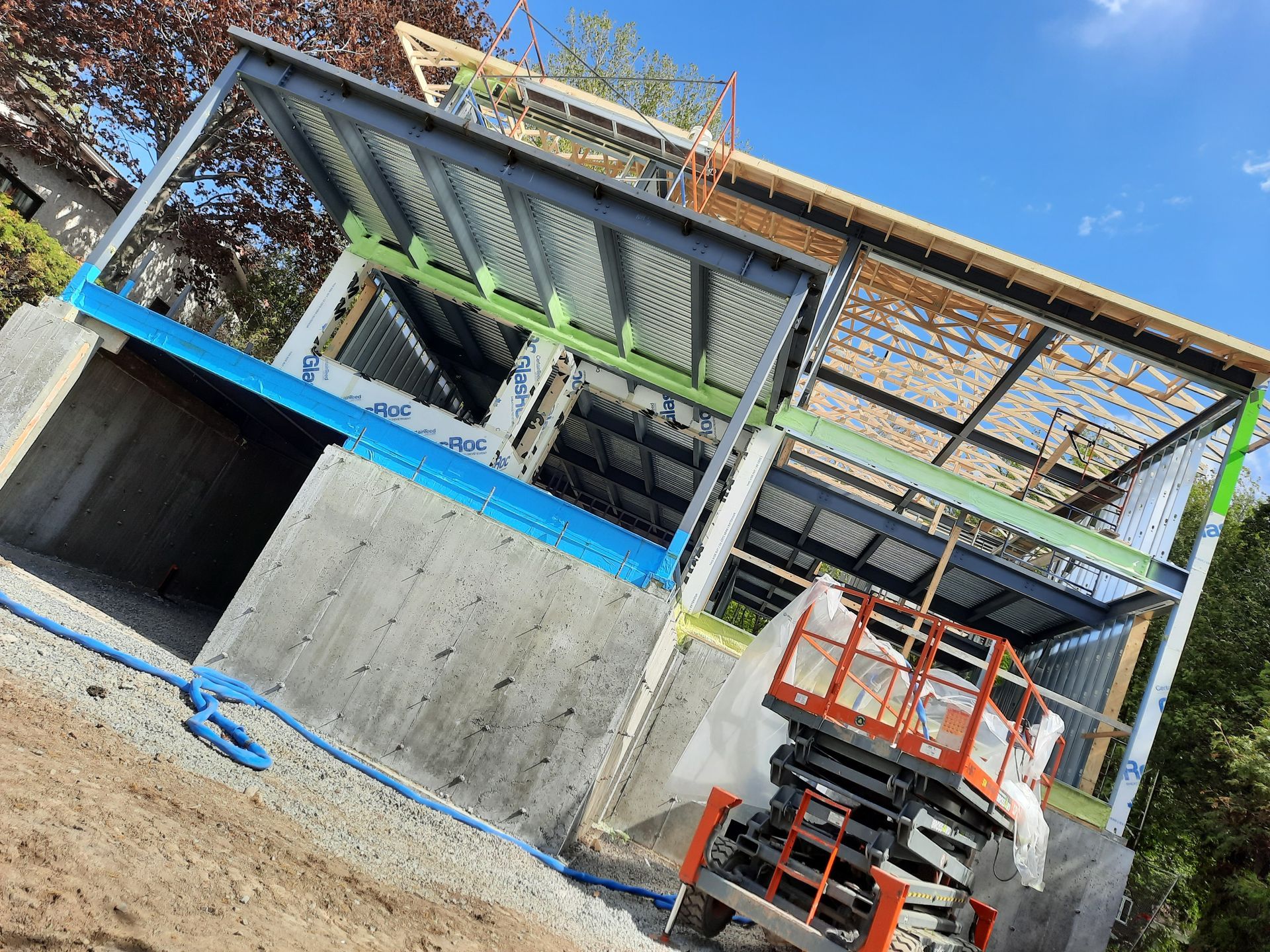 Chantier de construction avec base en béton, charpente en acier et élévateur. Ciel bleu en arrière-plan.