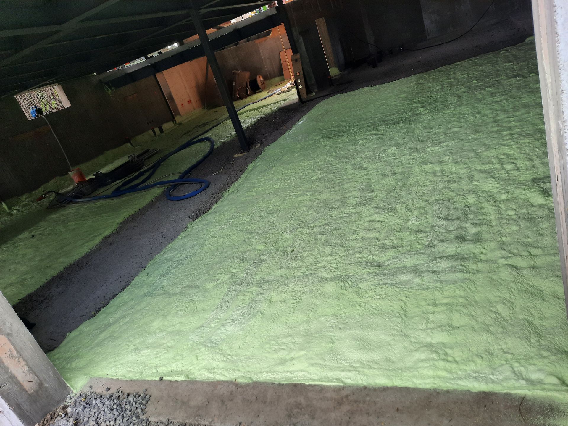 Isolation en mousse pulvérisée verte sur un sol en béton dans un espace sombre et non fini.