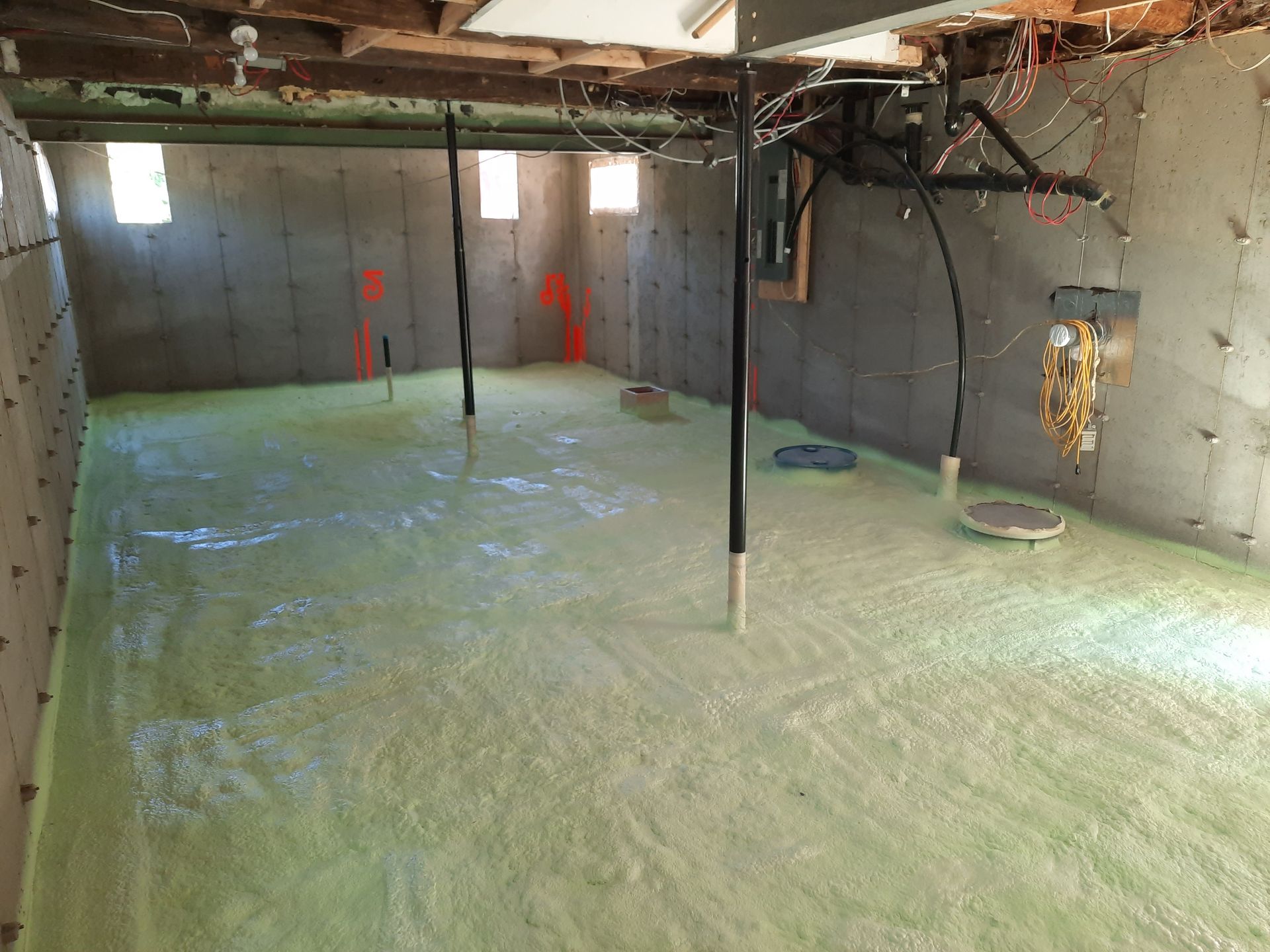 Sous-sol avec isolation en mousse verte sur le sol et les murs, poutres de soutien et quelques petites fenêtres.
