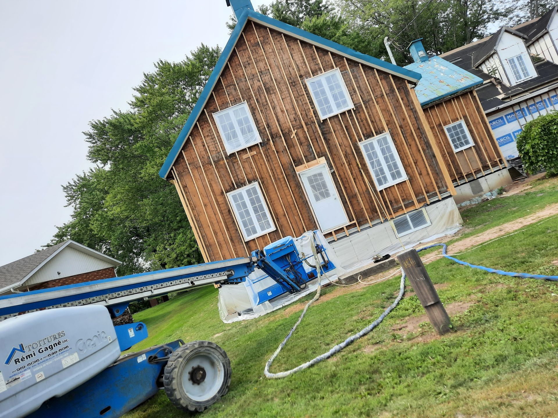 Une maison soulevée par un ascenseur bleu sur une pelouse herbeuse, avec des arbres en arrière-plan.
