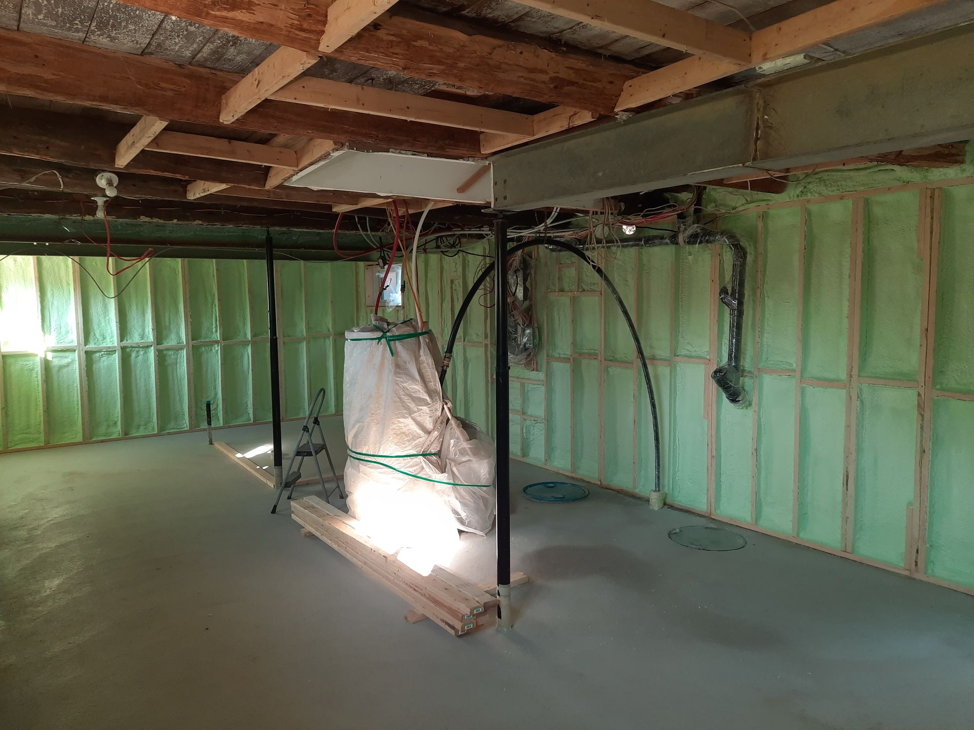 Rénovation du sous-sol en cours. Isolation écologique, plancher en béton gris, poutres apparentes et poutres de soutien.