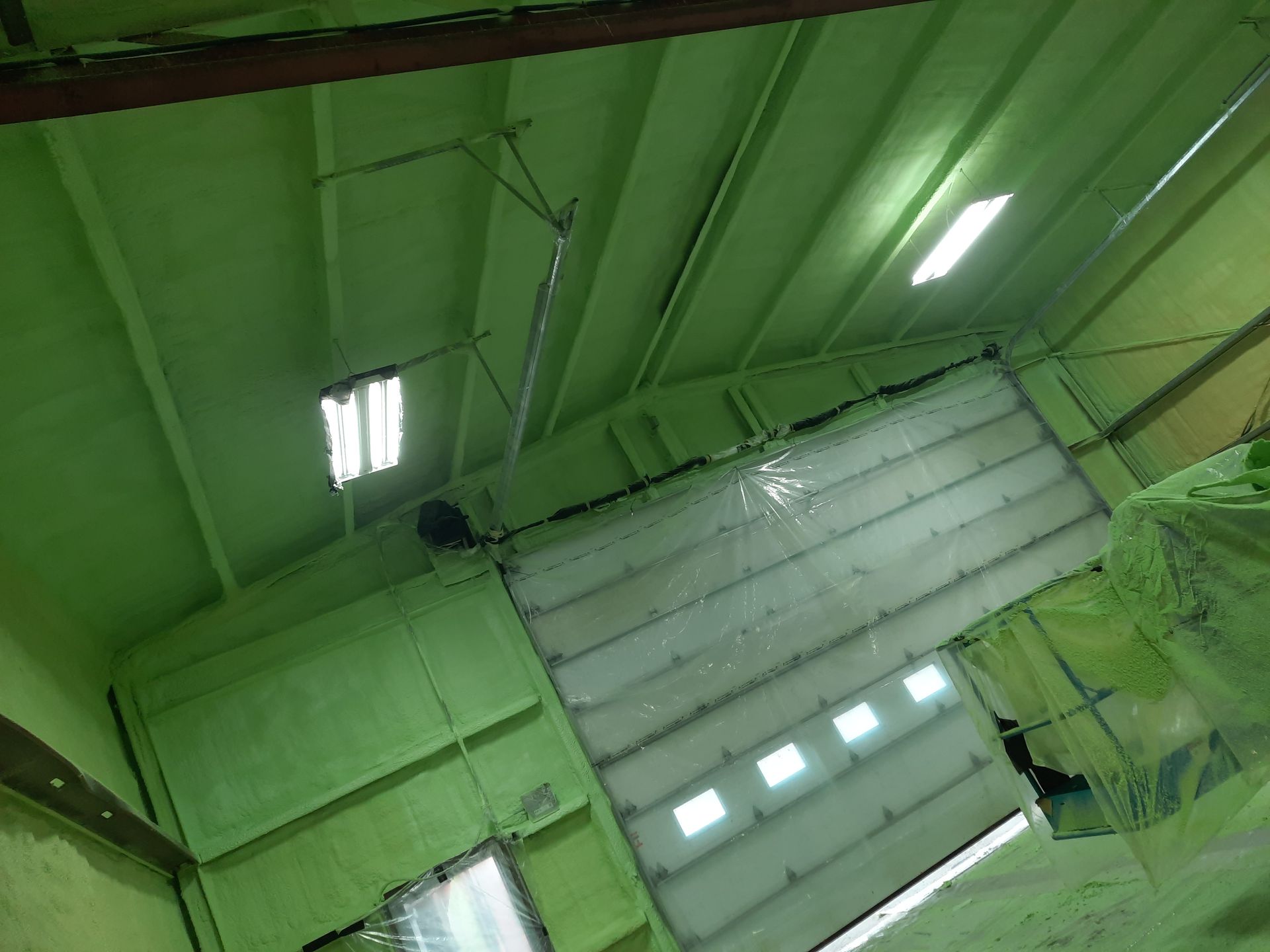 Intérieur d'entrepôt peint en vert avec une grande porte basculante et des lumières fluorescentes.