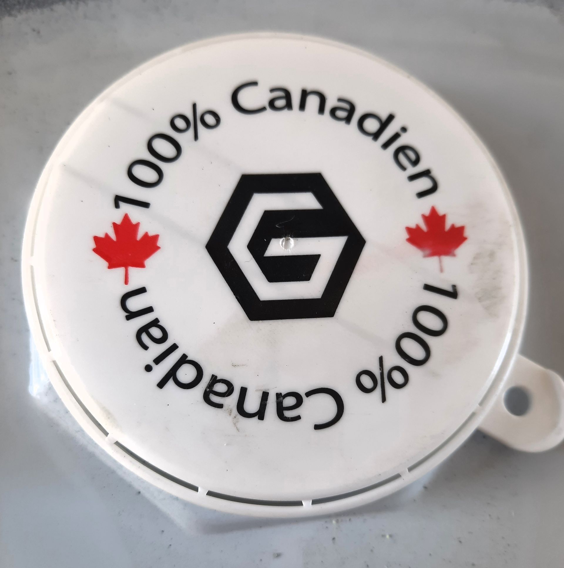 Couvercle circulaire blanc avec texte « 100 % canadien », feuilles d'érable rouges et logo hexagonal noir.