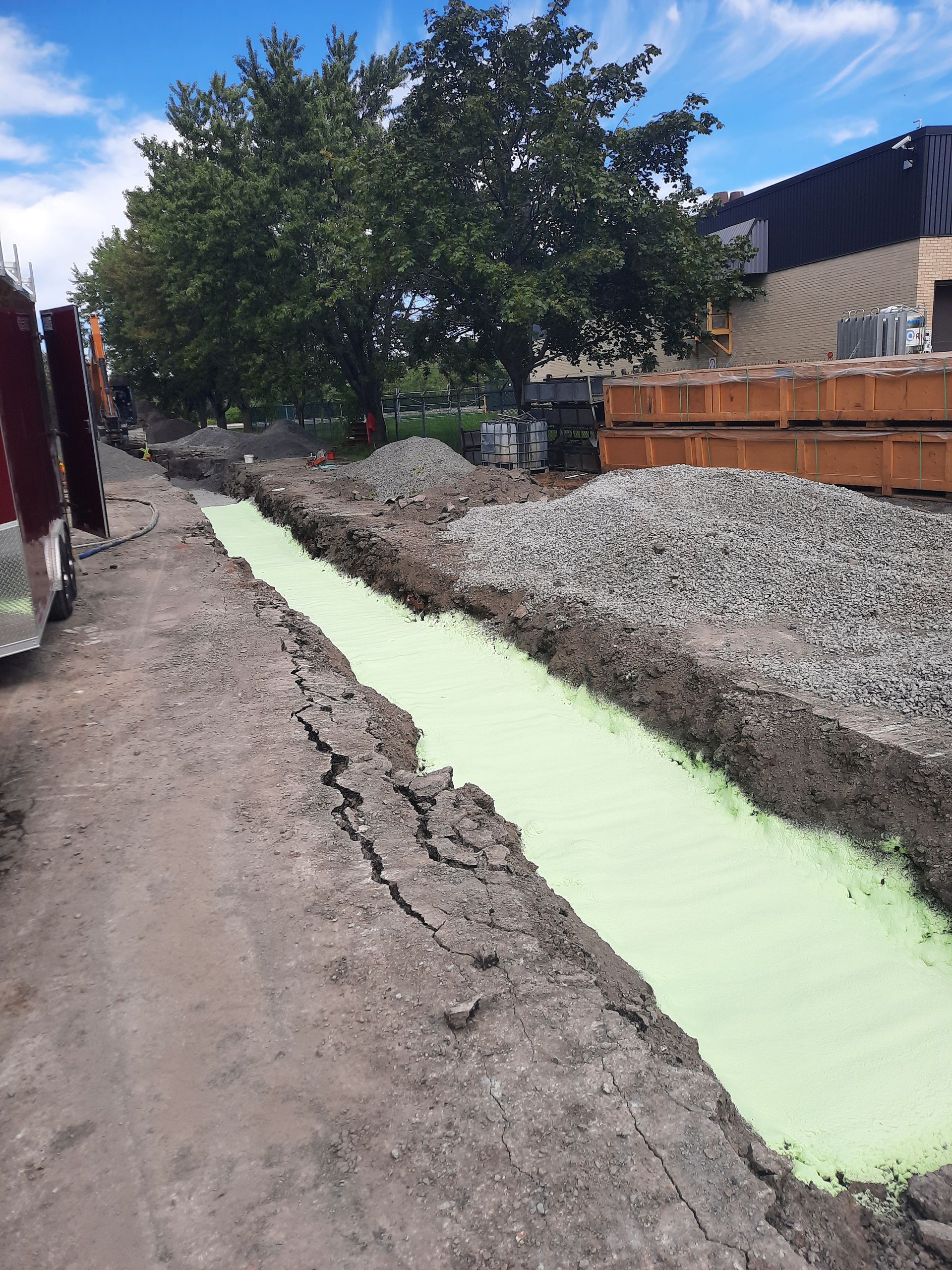 Chantier : Tranchée enrobée de matériaux verts, entourée de terre, gravier et matériaux.