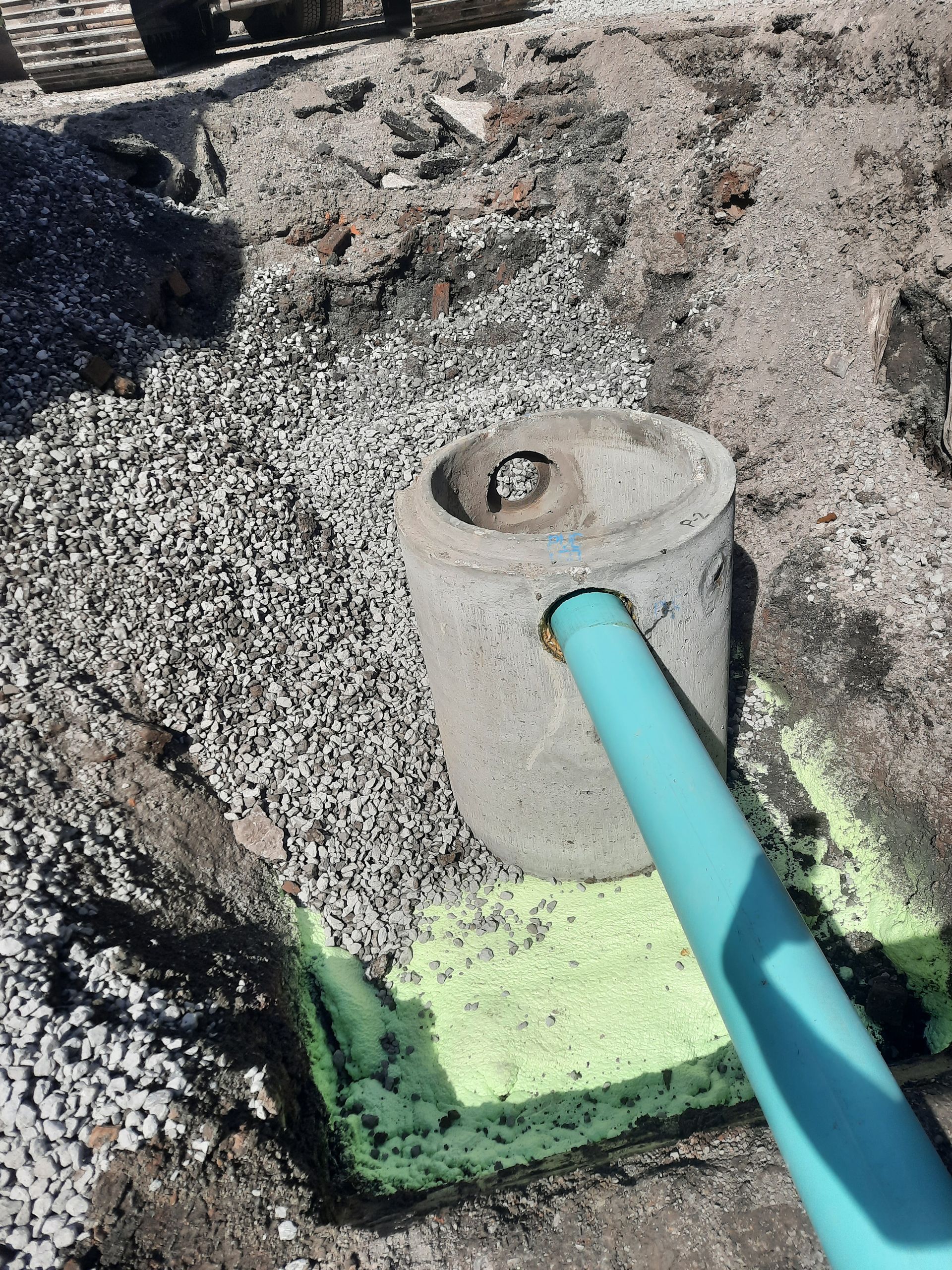 Un puits en béton avec un tuyau bleu débouchant dans une tranchée remplie de gravier. Le sol est marqué de peinture jaune.