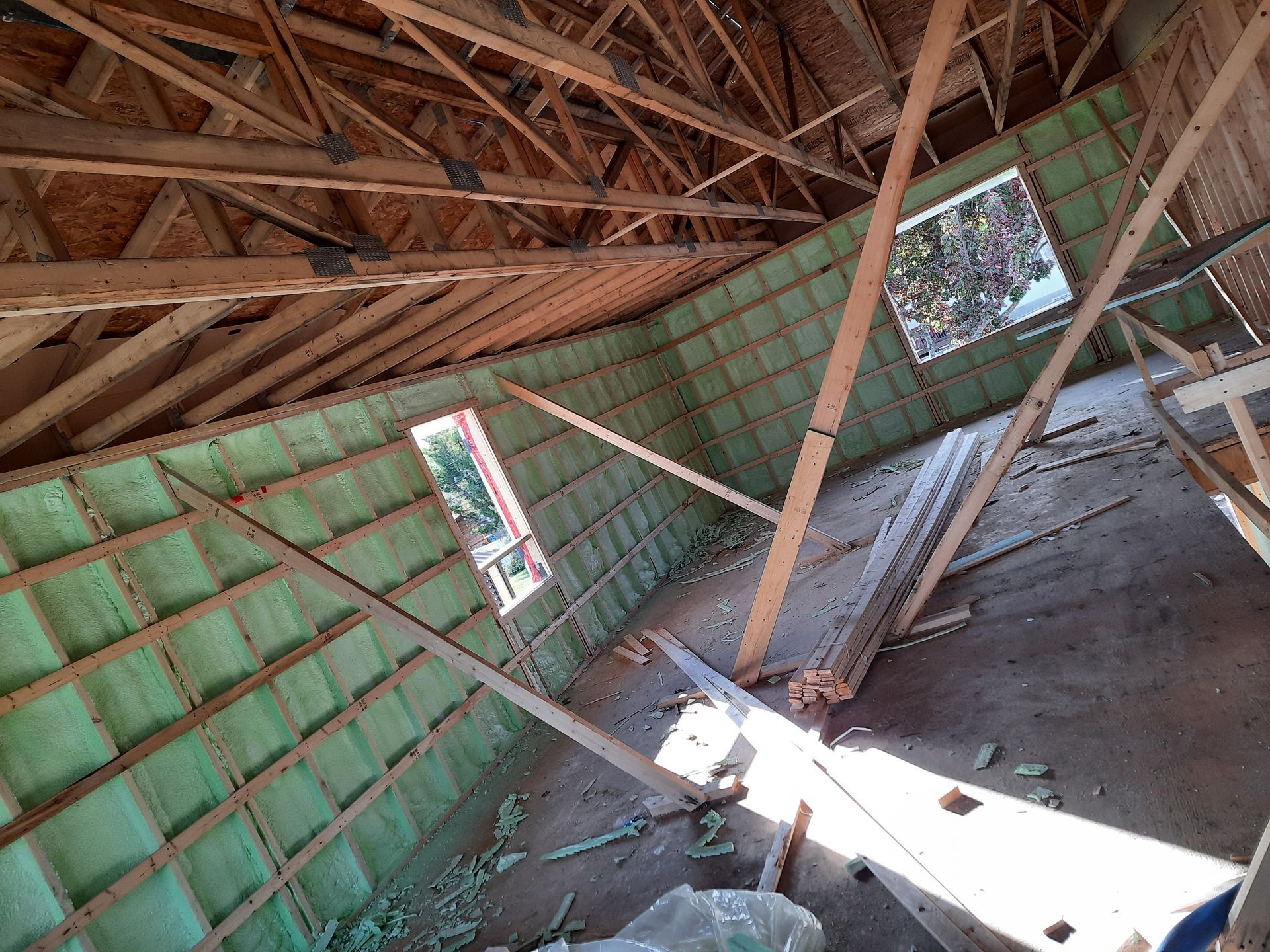 Vue intérieure d'un bâtiment en construction, montrant des poutres en bois, une isolation verte et des cadres de fenêtres.
