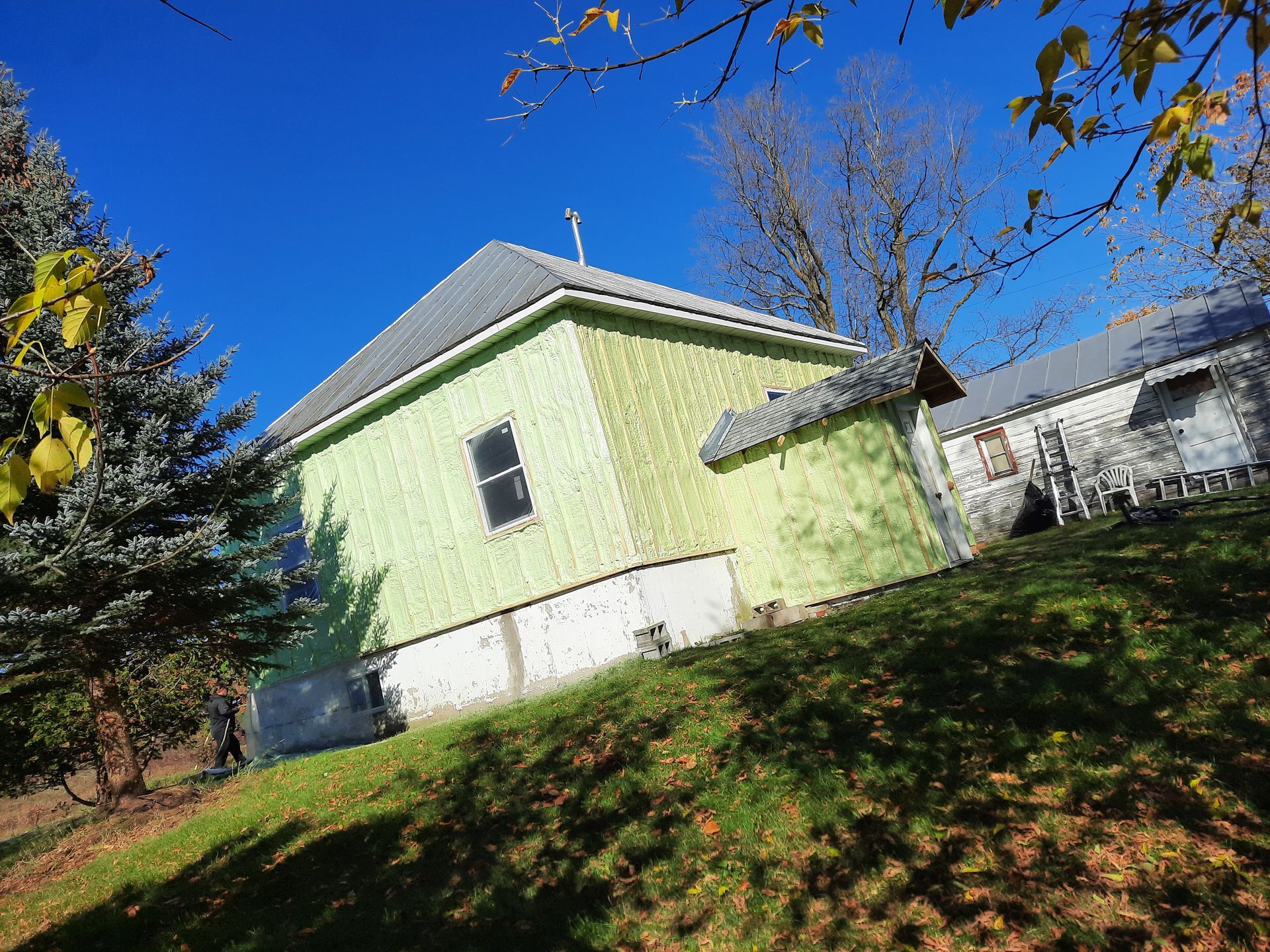 Bâtiment vert sur une colline herbeuse contre un ciel bleu vif, avec des arbres.