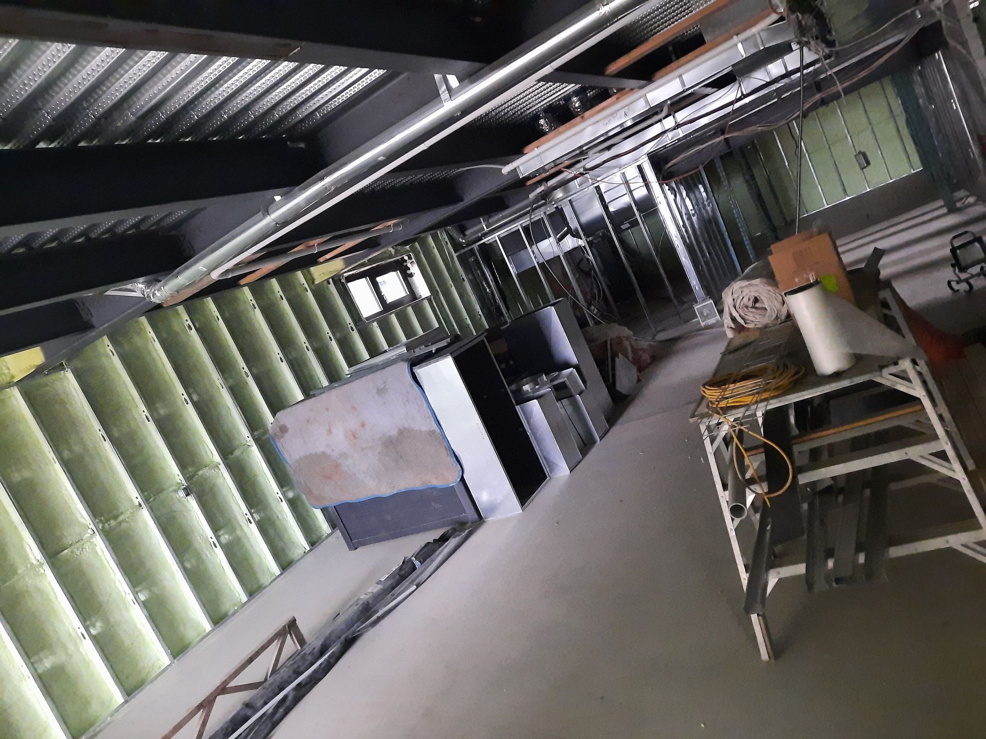 Chantier intérieur avec poutres métalliques, murs gris et jaunes et une échelle.