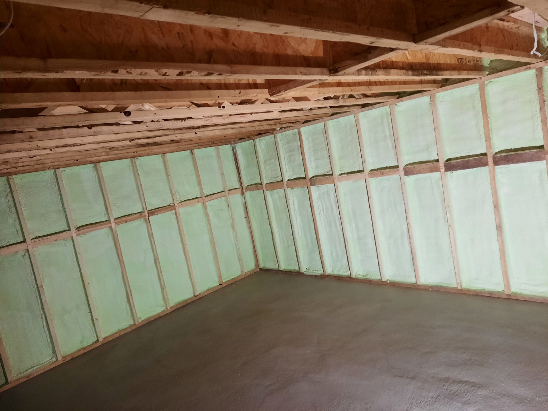 Vue intérieure d'une pièce en construction, murs avec isolation verte, ossature bois et sol en béton.