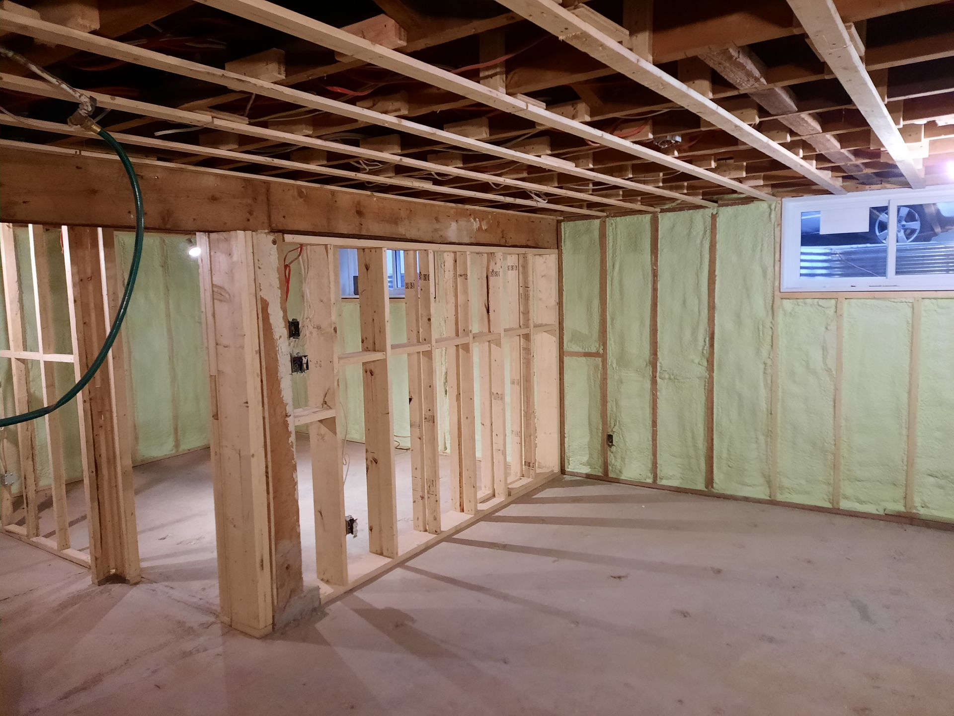 Charpente du sous-sol avec isolation en mousse projetée. Poutres et montants en bois, plancher en béton.