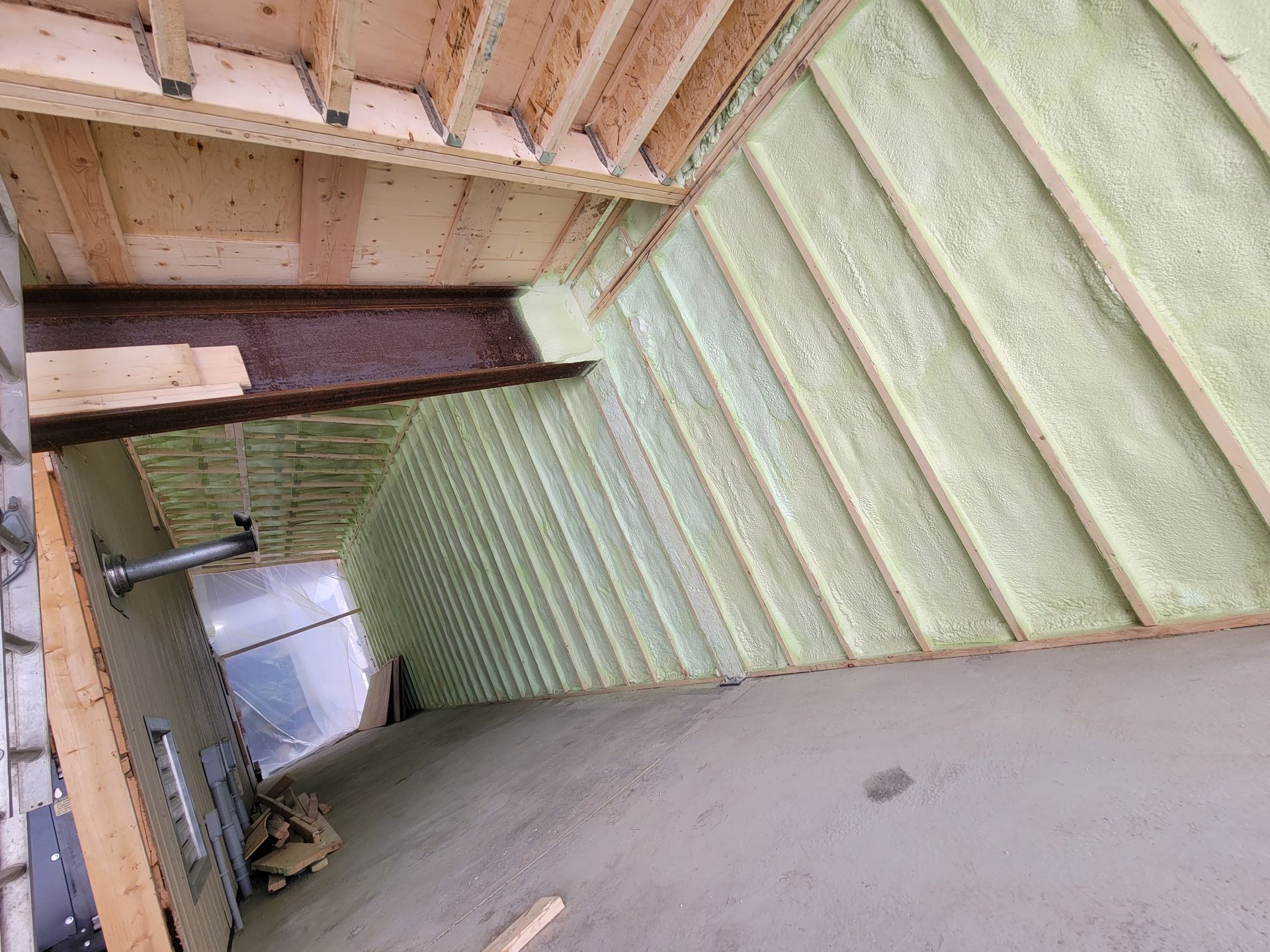 Vue intérieure d'un toit en construction, montrant l'isolation entre les poutres en bois, avec une surface en béton en dessous.