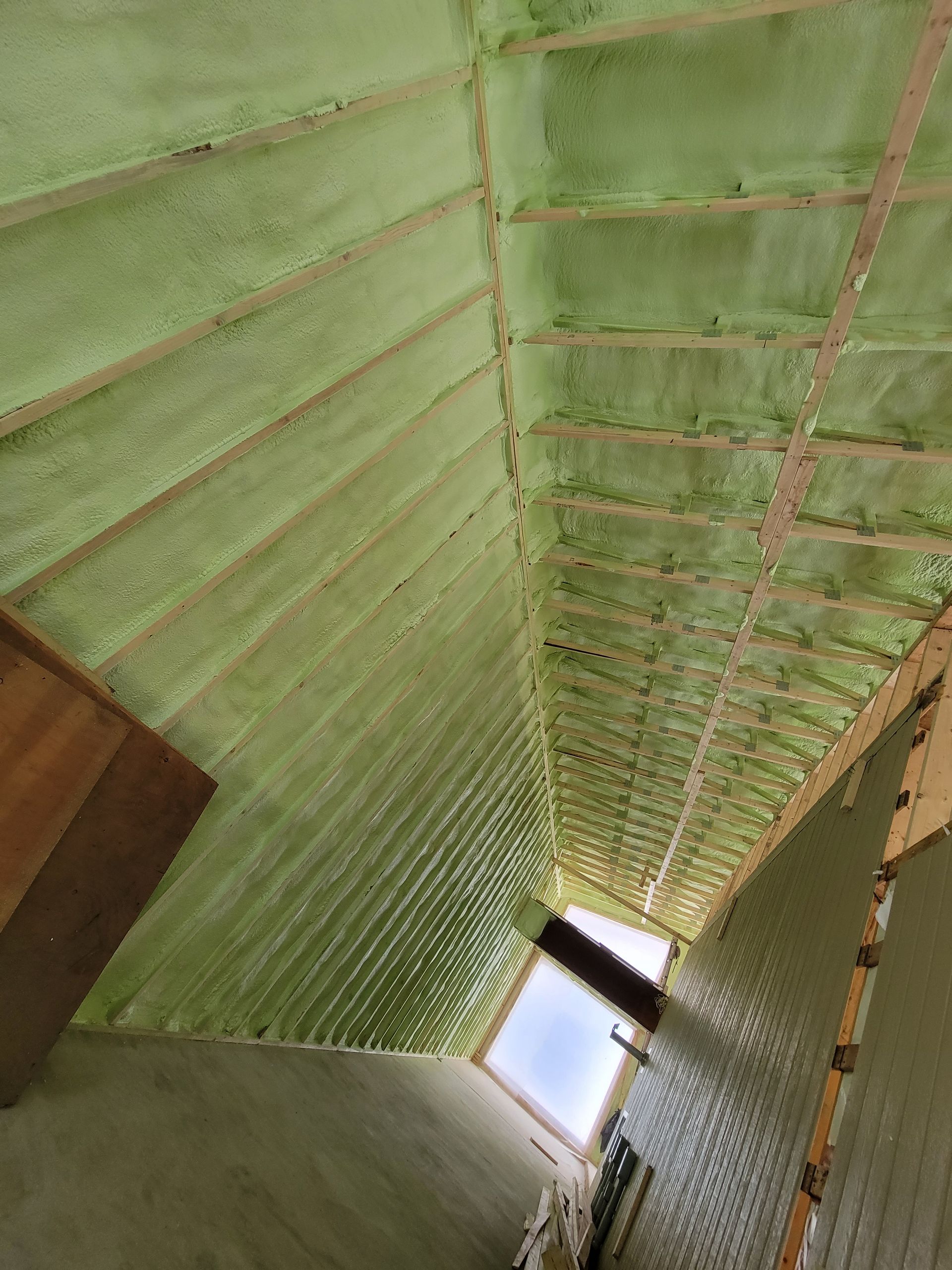 Isolation en mousse pulvérisée verte appliquée sur les chevrons du toit et le plafond d'un grenier.
