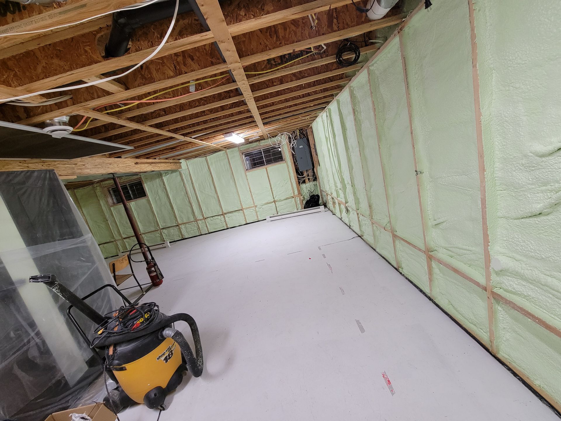 Sous-sol en construction avec murs isolés, un plancher blanc et un aspirateur jaune.