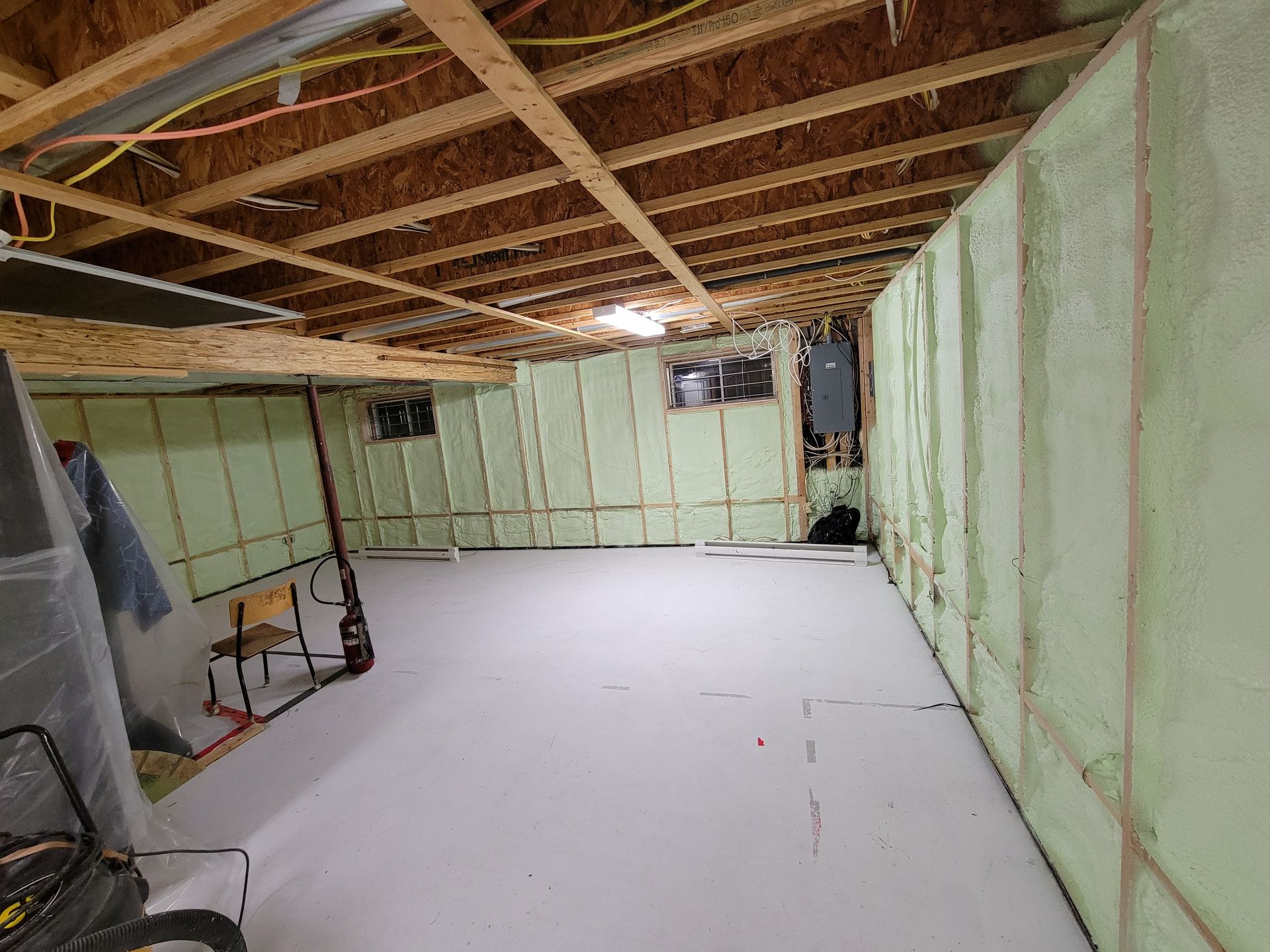 Sous-sol avec isolation verte sur les murs, poutres apparentes en bois et plancher gris clair, partiellement fini.